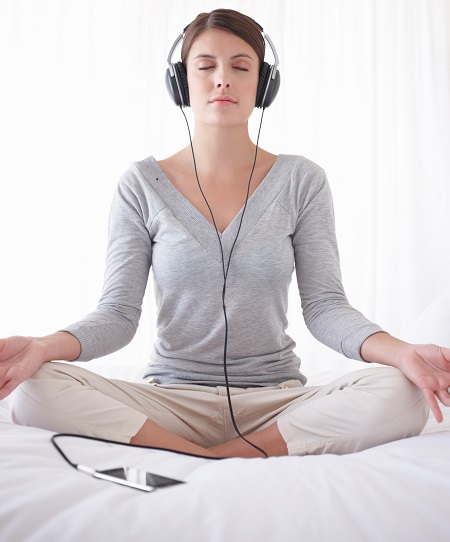 Pretty girl with headphones sitting in lotus position on bed